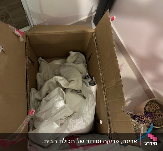 קופסה פתוחה עם בגדים וניירות על הרצפה